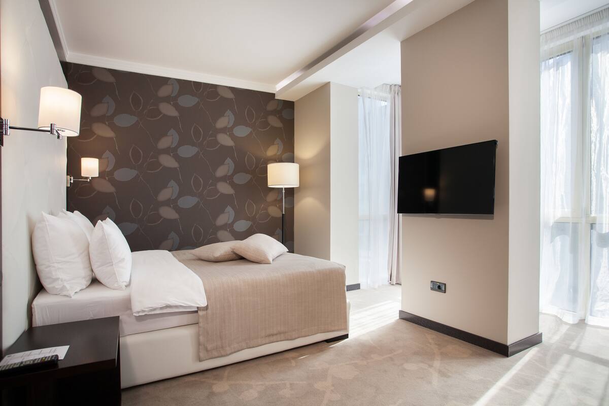 A modern hotel room with a bed, a flat-screen TV, and a wall-mounted lamp.