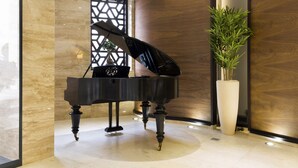 A grand piano in a modern lobby with marble flooring, a wooden accent wall, and a large potted plant. - Constantine the Great (Belgrade)