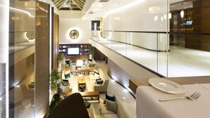 A modern hotel lobby with a seating area, a reception desk, and a dining setup with a plate and fork on a table. - Constantine the Great (Belgrade)