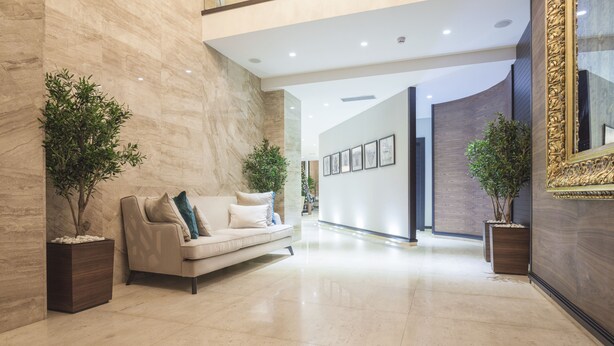 A spacious lobby with a marble floor, a beige sofa with cushions, and two potted plants. - Constantine the Great (Belgrade)