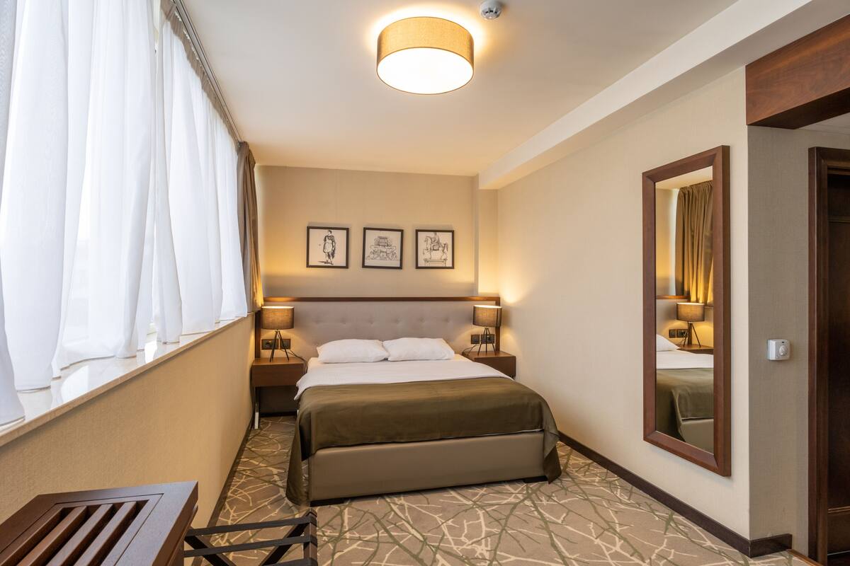 A hotel room with a bed, nightstands, a mirror, and artwork on the wall.