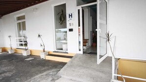 A hotel entrance with a concrete floor, a wooden ceiling, and a white exterior wall.