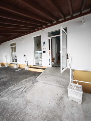 A hotel entrance with a concrete floor, a wooden ceiling, and a white exterior wall.