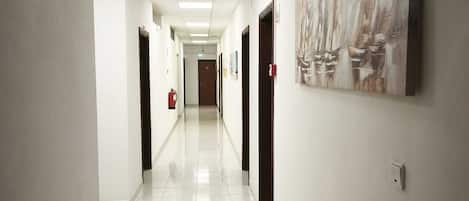 A long, narrow hallway with white walls, tiled floors, and doors on both sides.
