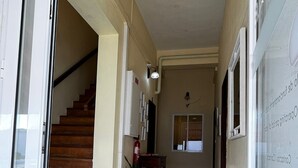 A hallway with a staircase, a fire extinguisher, a potted plant, and a doormat. - Hotel J.S.F. (Horta)