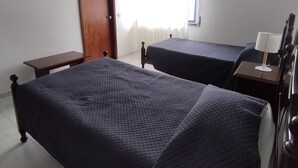 A hotel room with two beds, a desk, a chair, a TV mounted on the wall, and a window with curtains. - Hotel J.S.F. (Horta)