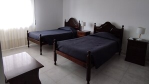 A hotel room with two wooden beds, a small table, and a bedside lamp.