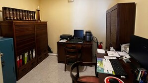A small office with a desk, computer, and filing cabinet. There is a chair and a small table with a phone and papers. - Hotel J.S.F. (Horta)