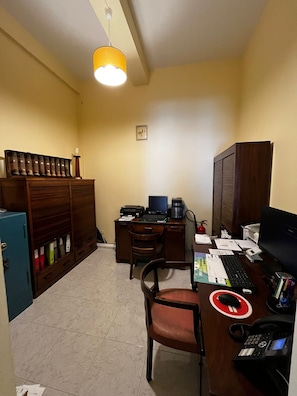 A small office with a desk, computer, and filing cabinet. There is a chair and a small table with a phone and papers. - Hotel J.S.F. (Horta)