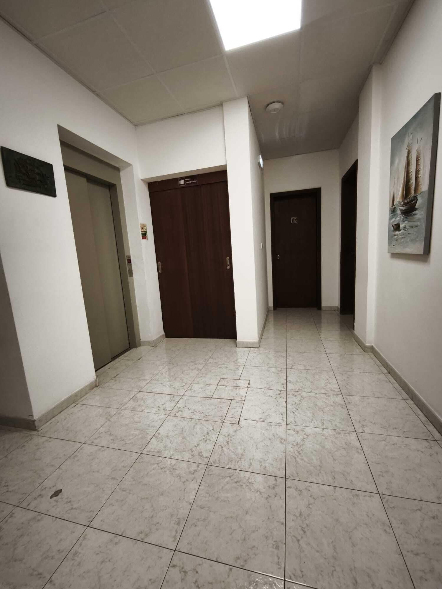 A corridor with tiled flooring, a wooden door, and a painting on the wall.