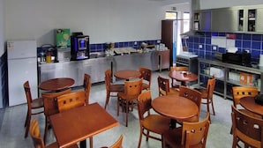 A restaurant with wooden tables and chairs, a kitchen area, and a blue tiled backsplash.