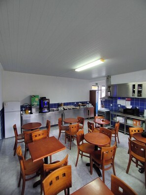 A restaurant with wooden tables and chairs, a kitchen area, and a blue tiled backsplash.