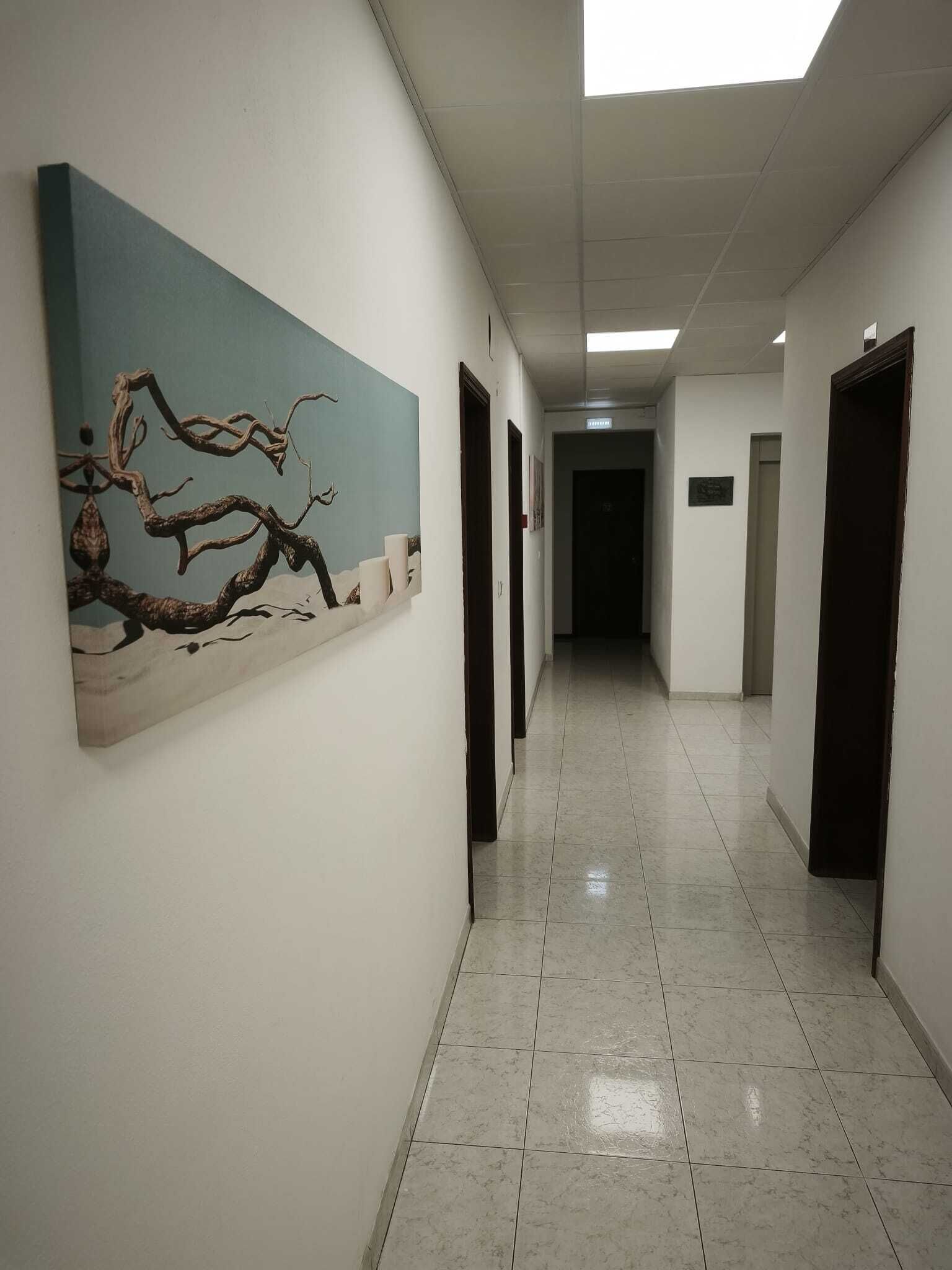 A corridor with a tiled floor, a painting on the left wall, and doors on both sides.
