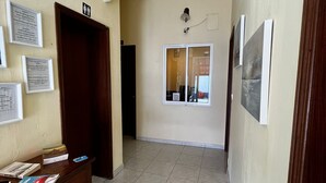 A hallway with a wooden desk, framed notices, and a door. - Hotel J.S.F. (Horta)