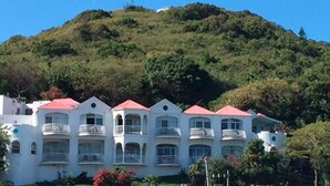 A multi-story hotel with a red roof, surrounded by lush greenery and hills. - Fort Burt Hotel (Road Town)