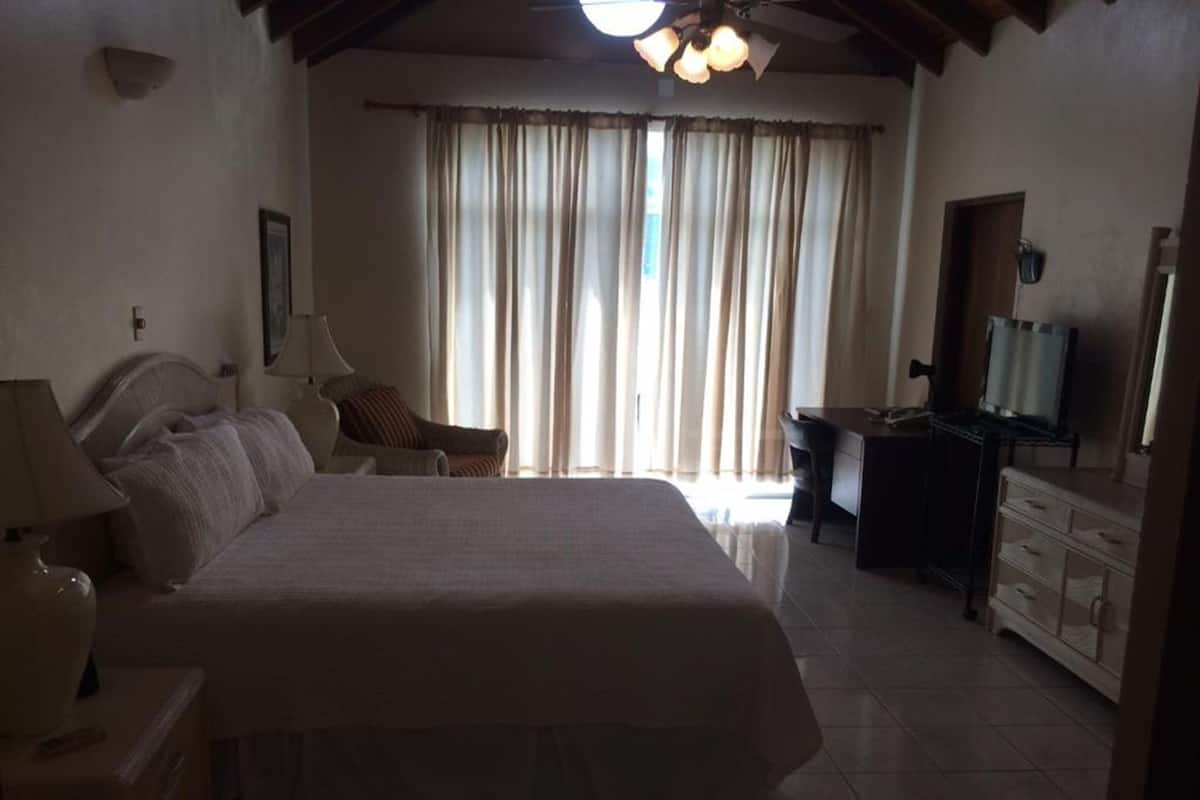Quarto de hotel com uma cama grande, uma escrivaninha, uma cadeira, uma televisão e uma janela com cortinas.