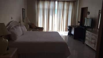 Een hotelkamer met een groot bed, een bureau, een stoel, een televisie en een raam met gordijnen.