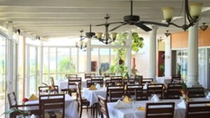 A restaurant with tables and chairs arranged under a covered area with a ceiling fan. - Fort Burt Hotel (Road Town)