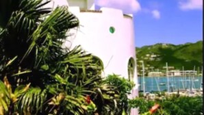 A white building with a pink roof, surrounded by greenery and a clear blue sky. - Fort Burt Hotel (Road Town)