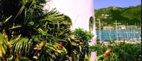 Un edificio blanco con techo rosa, rodeado de vegetación y un cielo azul despejado.