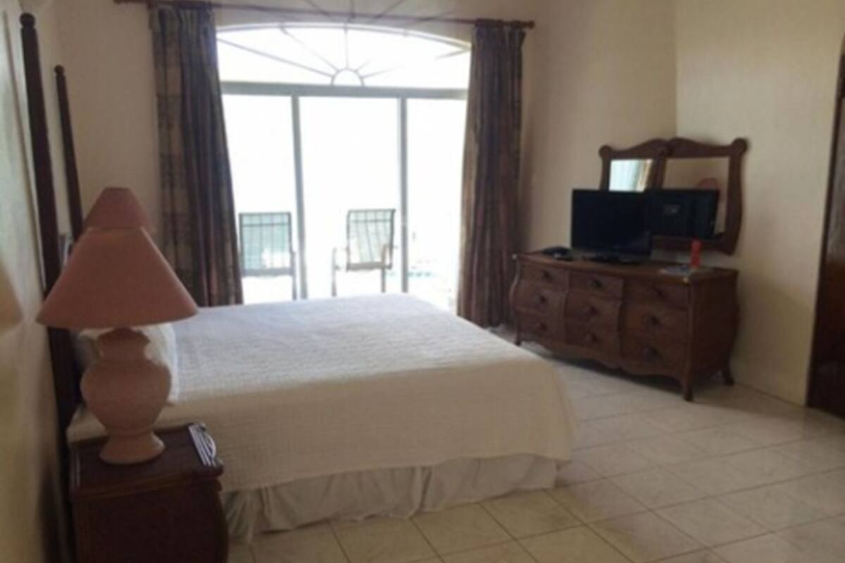 Quarto com cama, penteadeira, abajur e televisão.