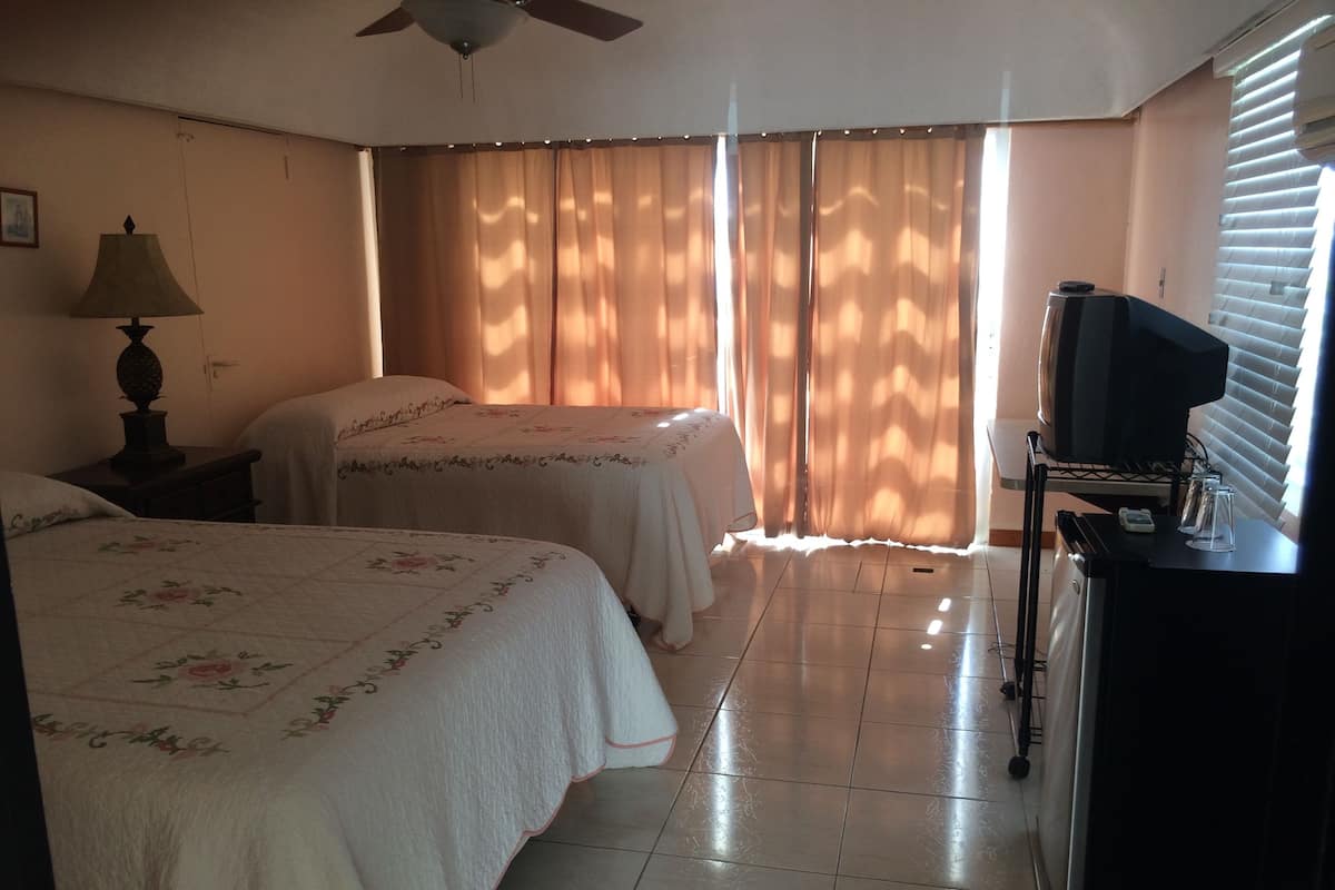 Quarto de hotel com duas camas, um ventilador de teto, televisão e minibar.