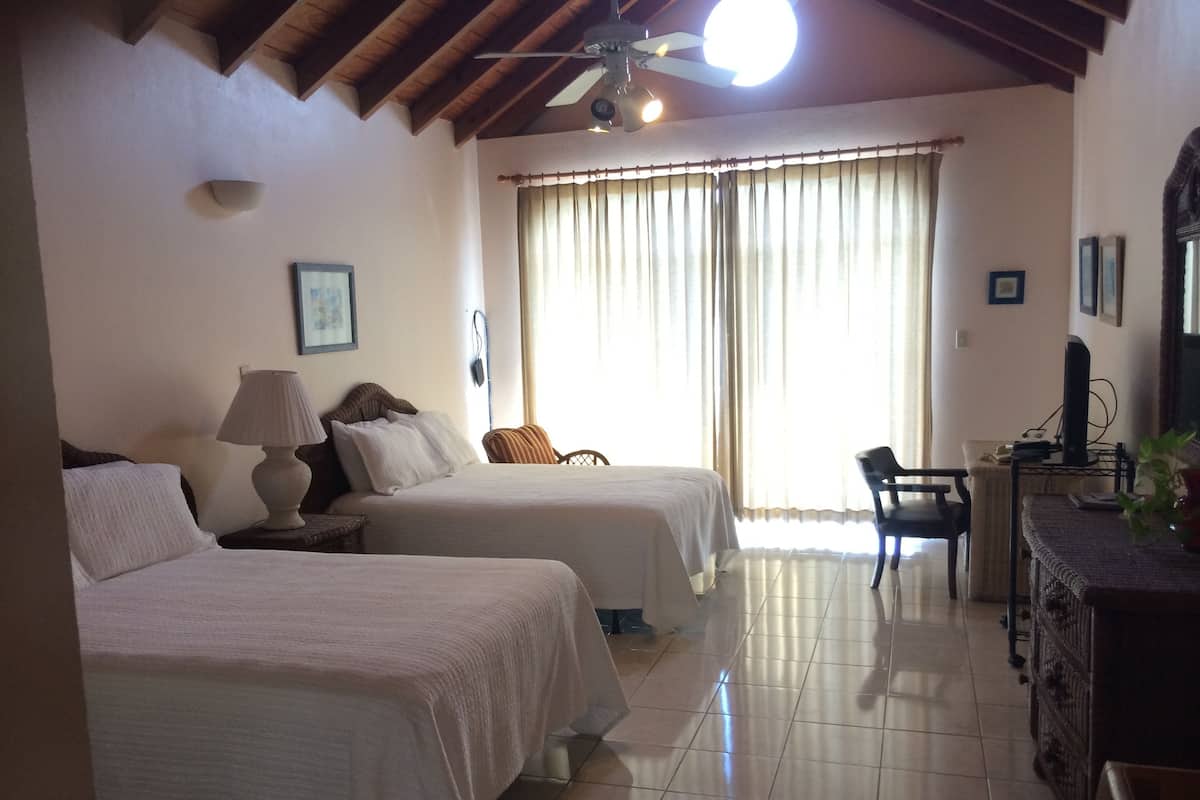 Quarto de hotel com duas camas, uma mesa de escritório com um computador, uma cadeira e um ventilador de teto.