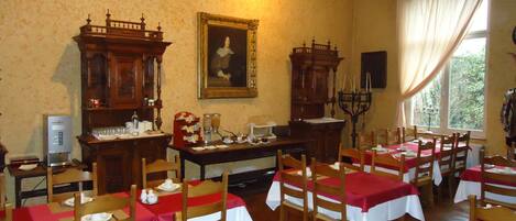 A dining area with wooden tables and chairs, a painting on the wall, and a large window with curtains.