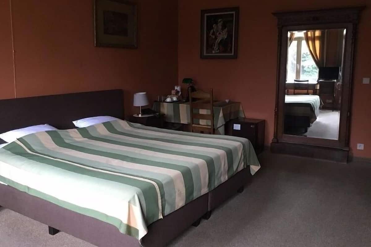 Una habitación de hotel con cama, escritorio, silla, lámpara y espejo.