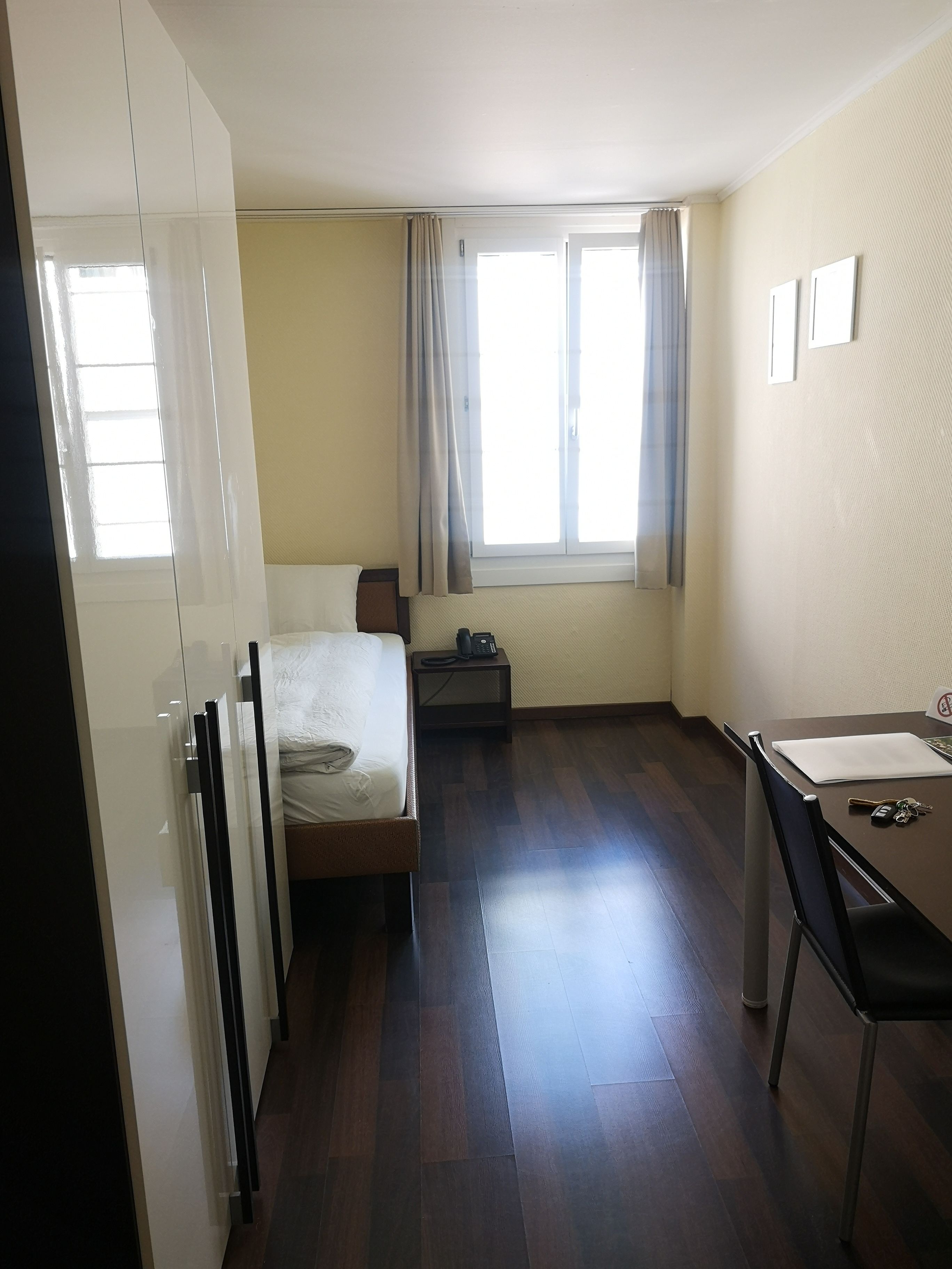 Habitación de hotel con cama, escritorio con silla, teléfono y ventana con cortinas.
