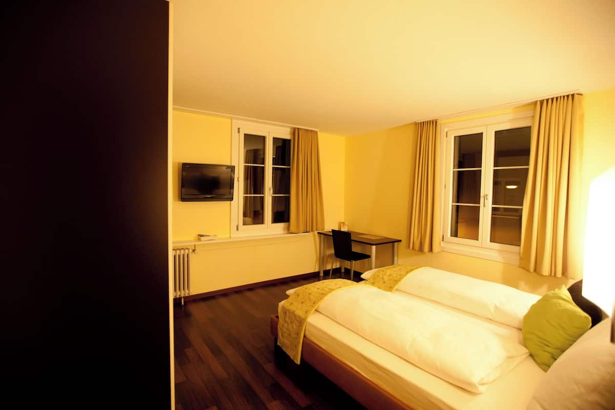 A hotel room with a bed, a desk, a chair, a television, and windows with curtains.