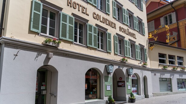 Un edificio con el letrero "HOTEL GOLDENER SCHLÜSSEL" y numerosas ventanas con contraventanas verdes.