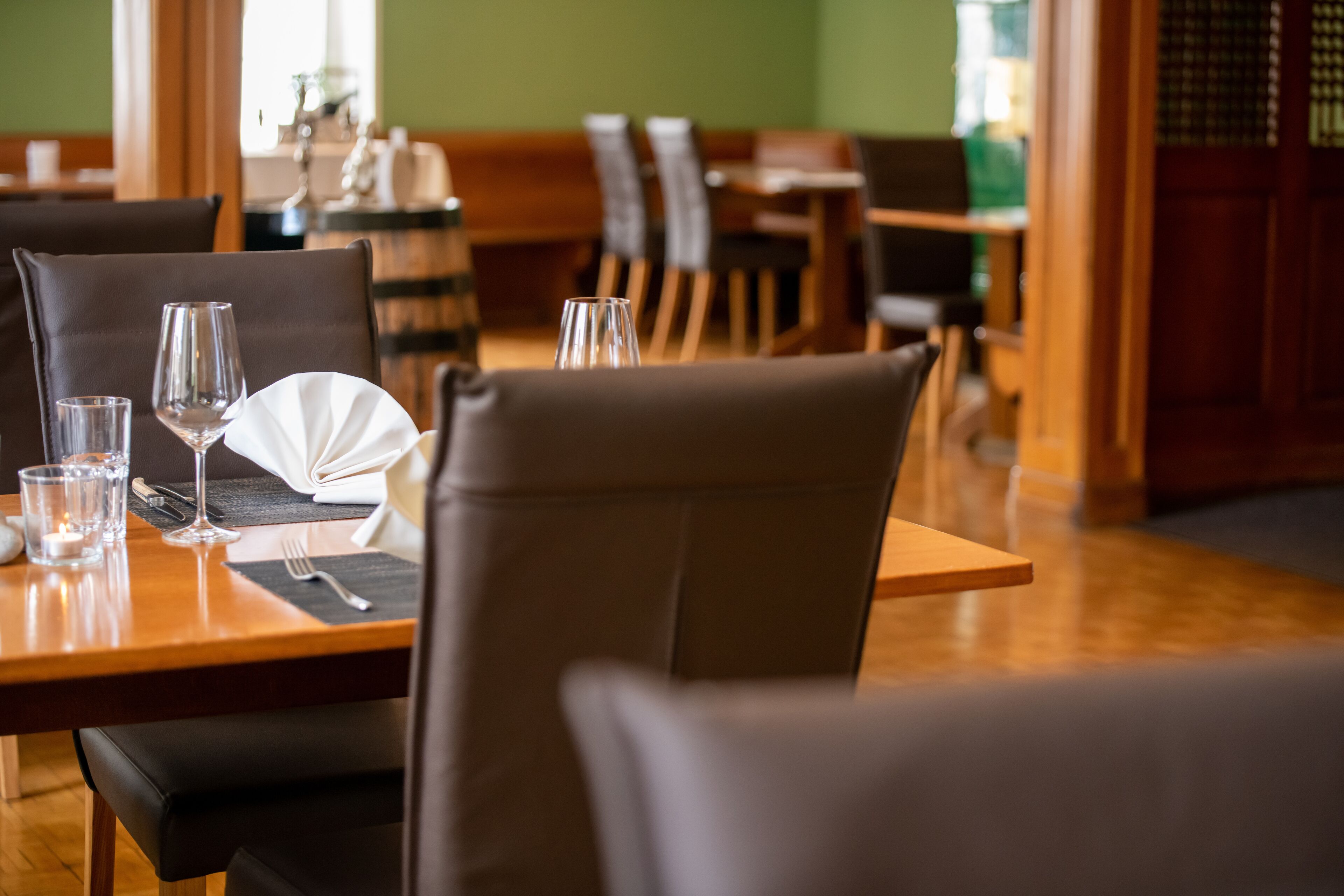 Un ambiente de restaurante con una mesa de madera dispuesta para dos personas, incluyendo un mantel blanco, dos copas de vino y cubiertos.