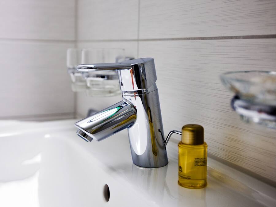 A modern bathroom with a chrome faucet, a glass soap dish, and a bottle of liquid soap.