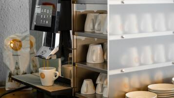 A coffee machine dispensing coffee into a cup, a stack of plates, and a tray of cups.