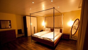 Una cama con dosel, suelo de madera, cómoda, mesita de noche y espejo.