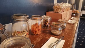Una mesa de buffet con diversos alimentos en frascos de vidrio, una caja de pan y un tazón de frutas.