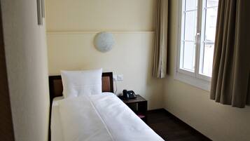 Une chambre d’hôtel avec un lit, une table de chevet avec un téléphone, une lampe fixée au mur et une fenêtre avec des rideaux.