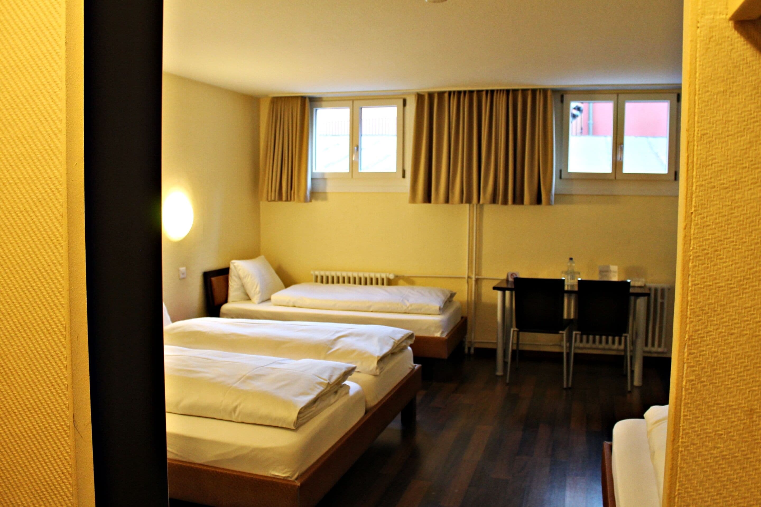 A hotel room with two single beds, a desk, and a chair.