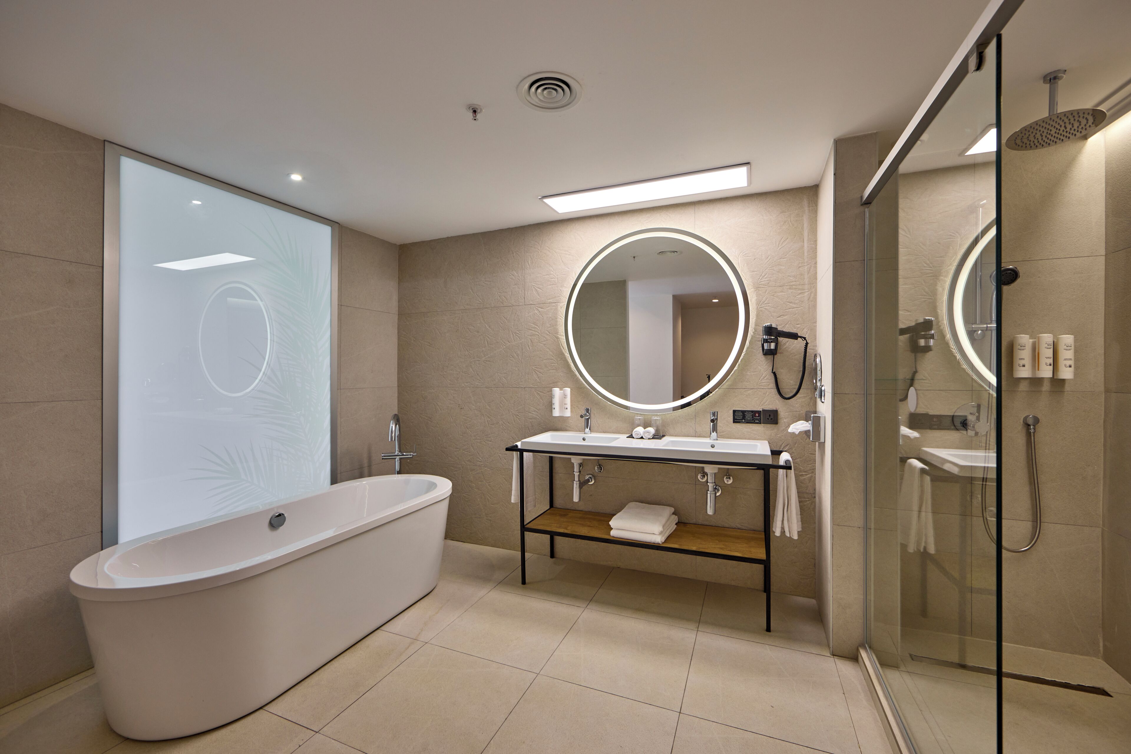 Un baño moderno con una bañera independiente, un espejo redondo sobre el lavamanos y una zona de ducha con paredes de vidrio.