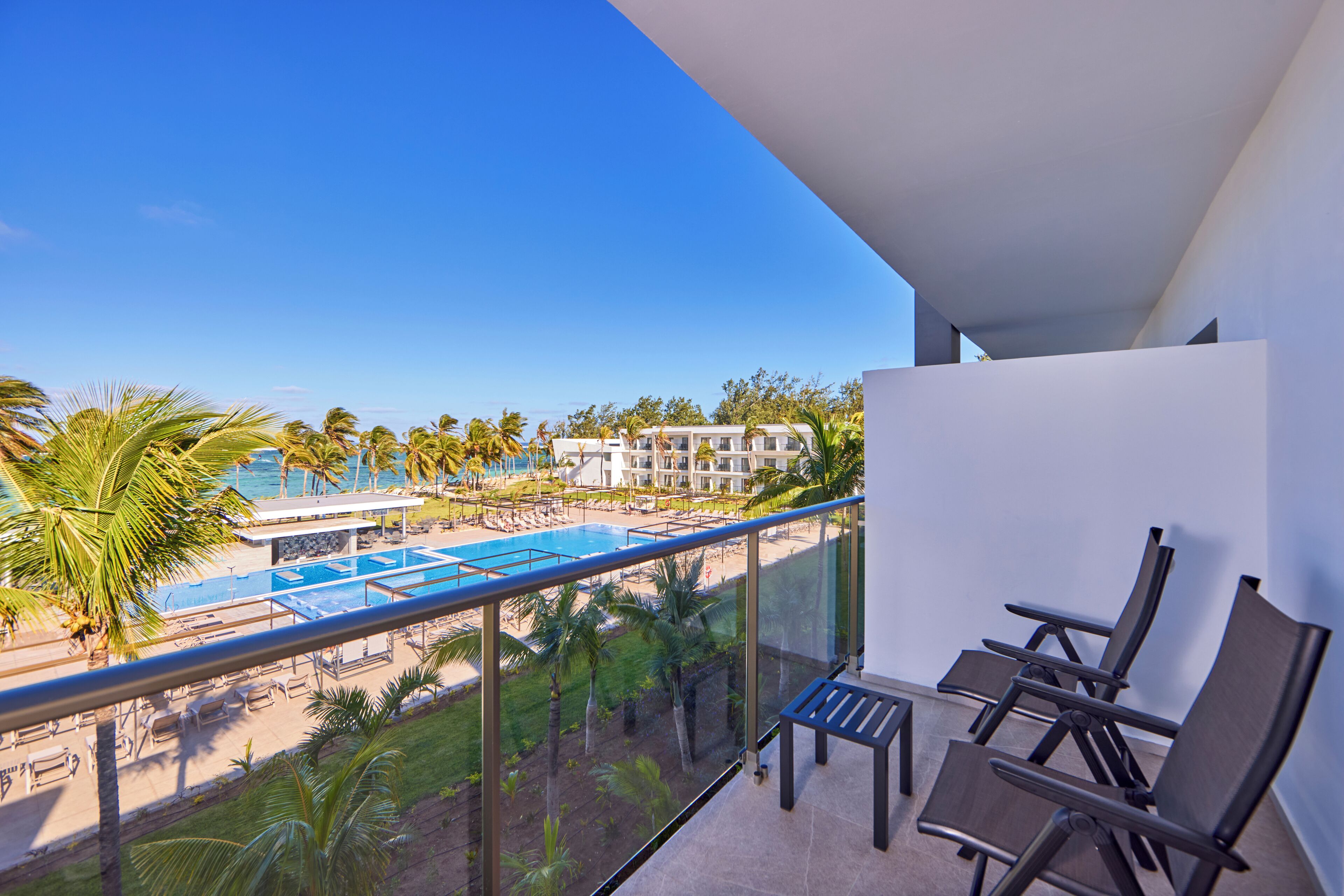 Un balcon avec vue sur une piscine et une plage, aménagé avec des chaises et une table.