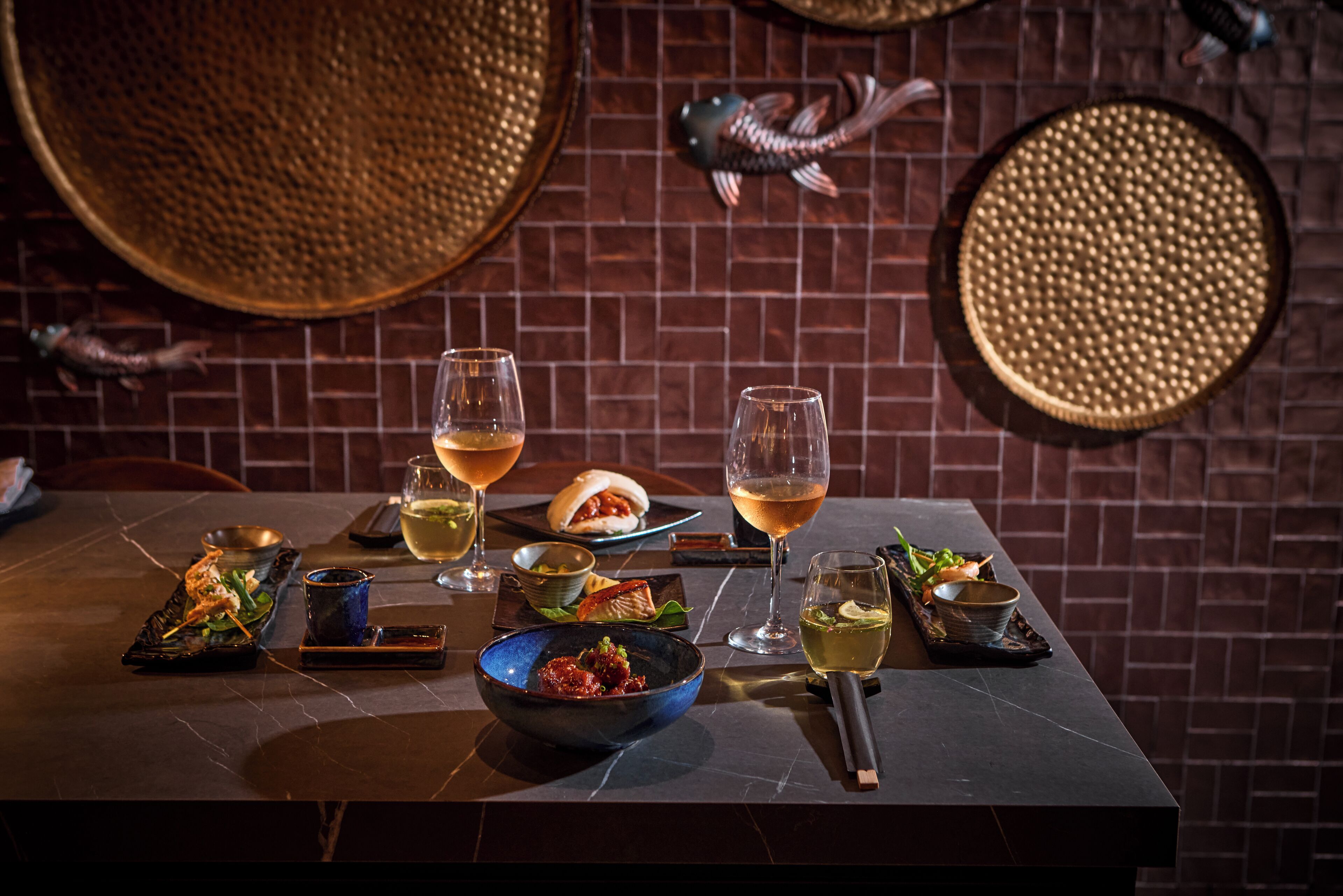 A dining table with various dishes, glasses of wine, and decorative elements like a fish sculpture and woven baskets.