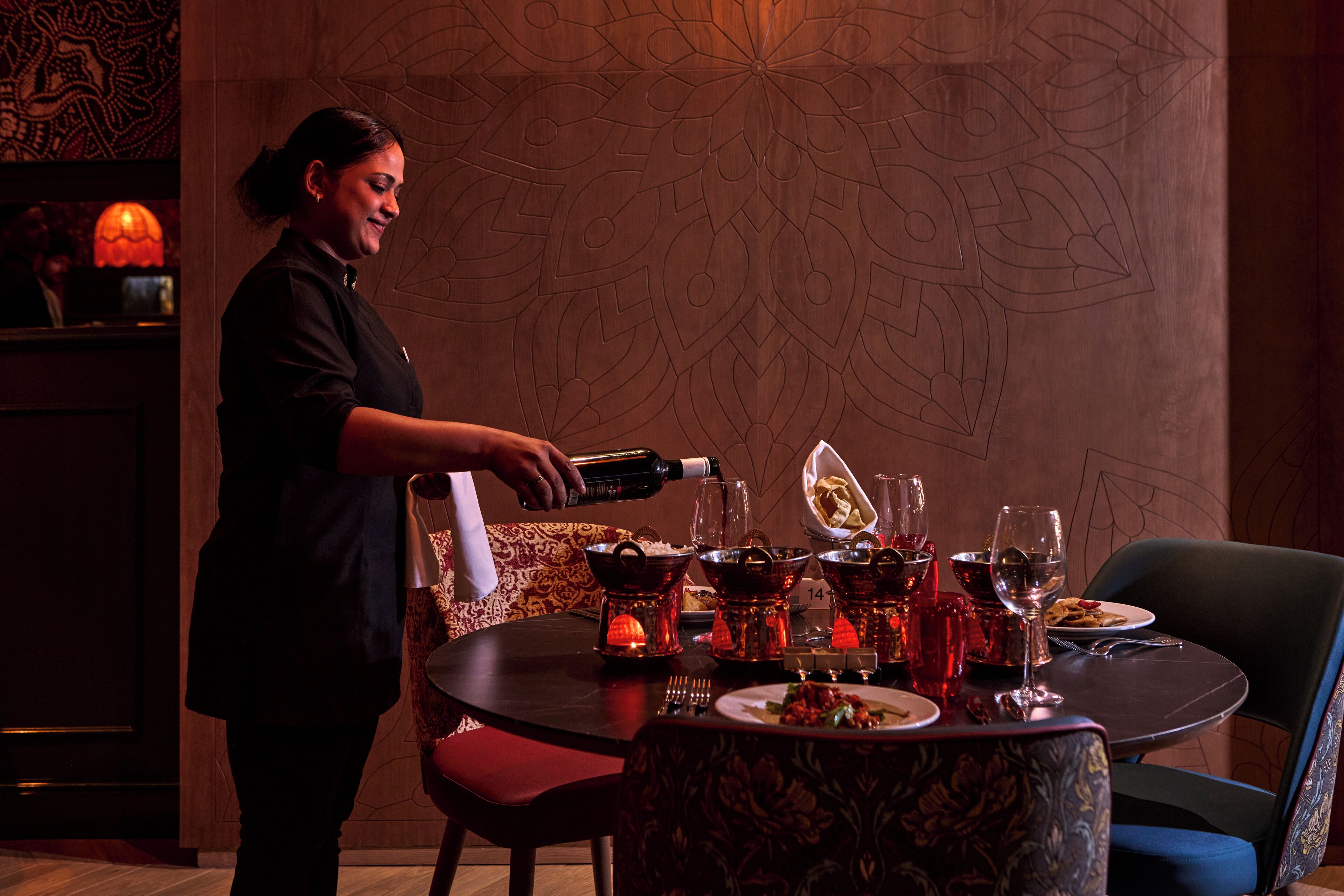 A bar area with a bartender pouring drinks, a table set with plates, glasses, and a bottle.
