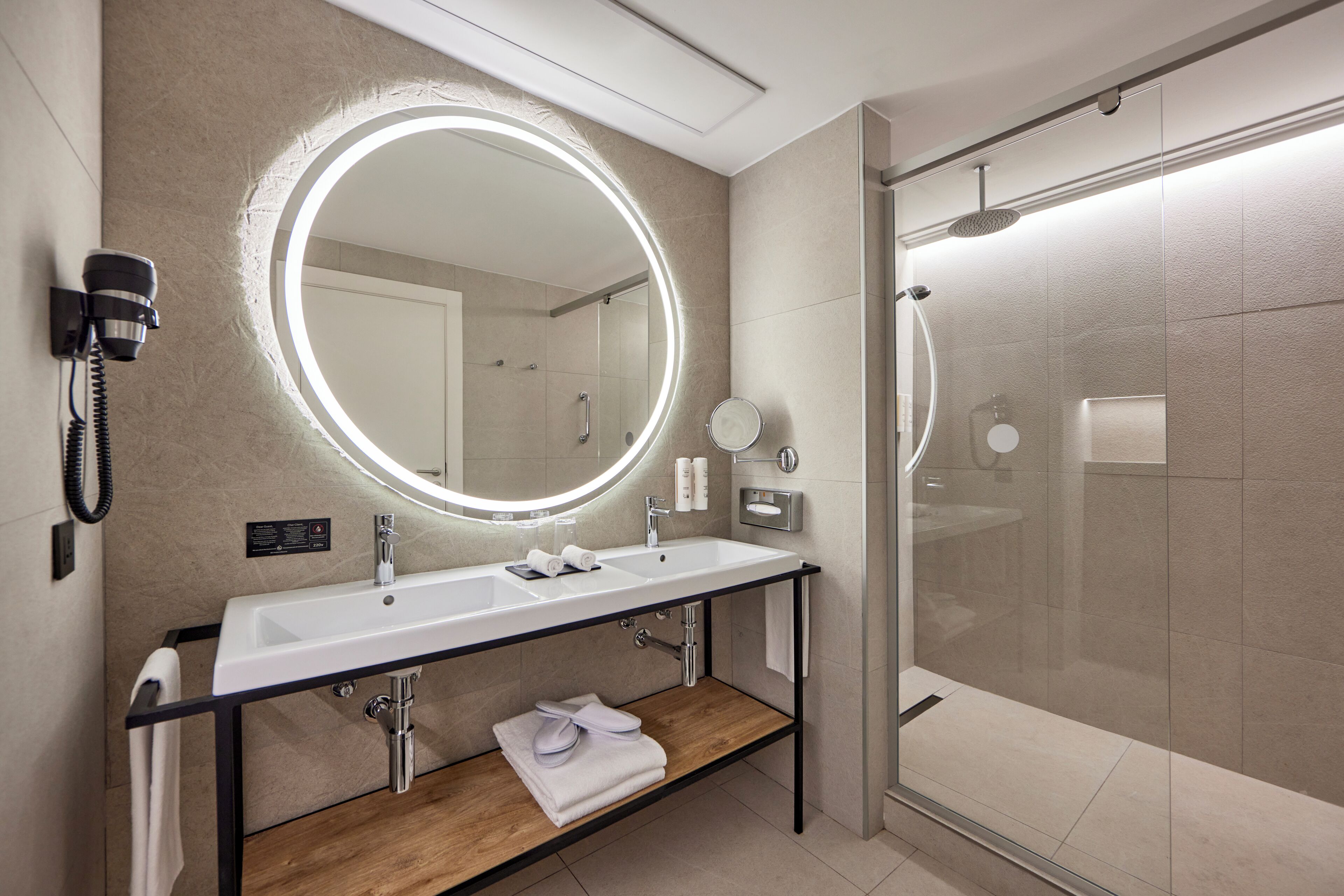 Une salle de bain moderne avec un double vasque, un grand miroir et une douche à parois de verre.