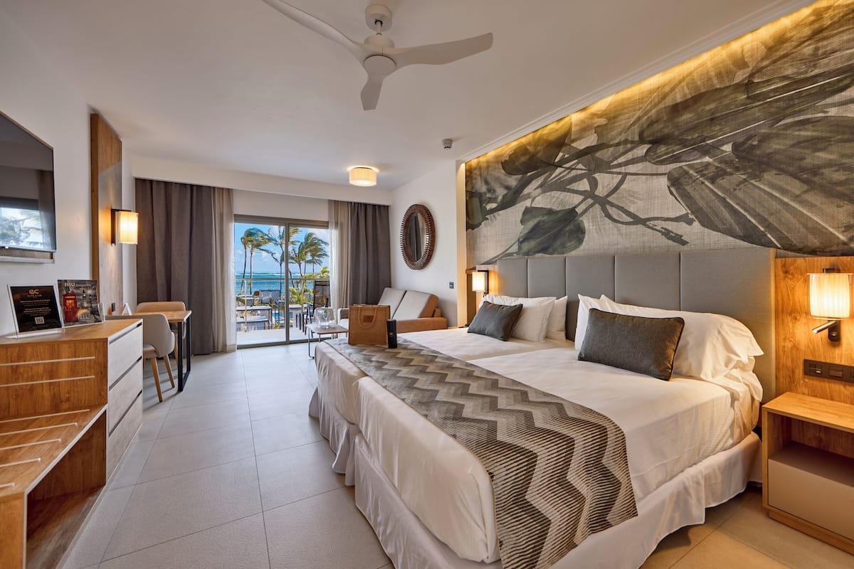 A hotel room with a large bed, a desk, and a view of palm trees and the ocean.