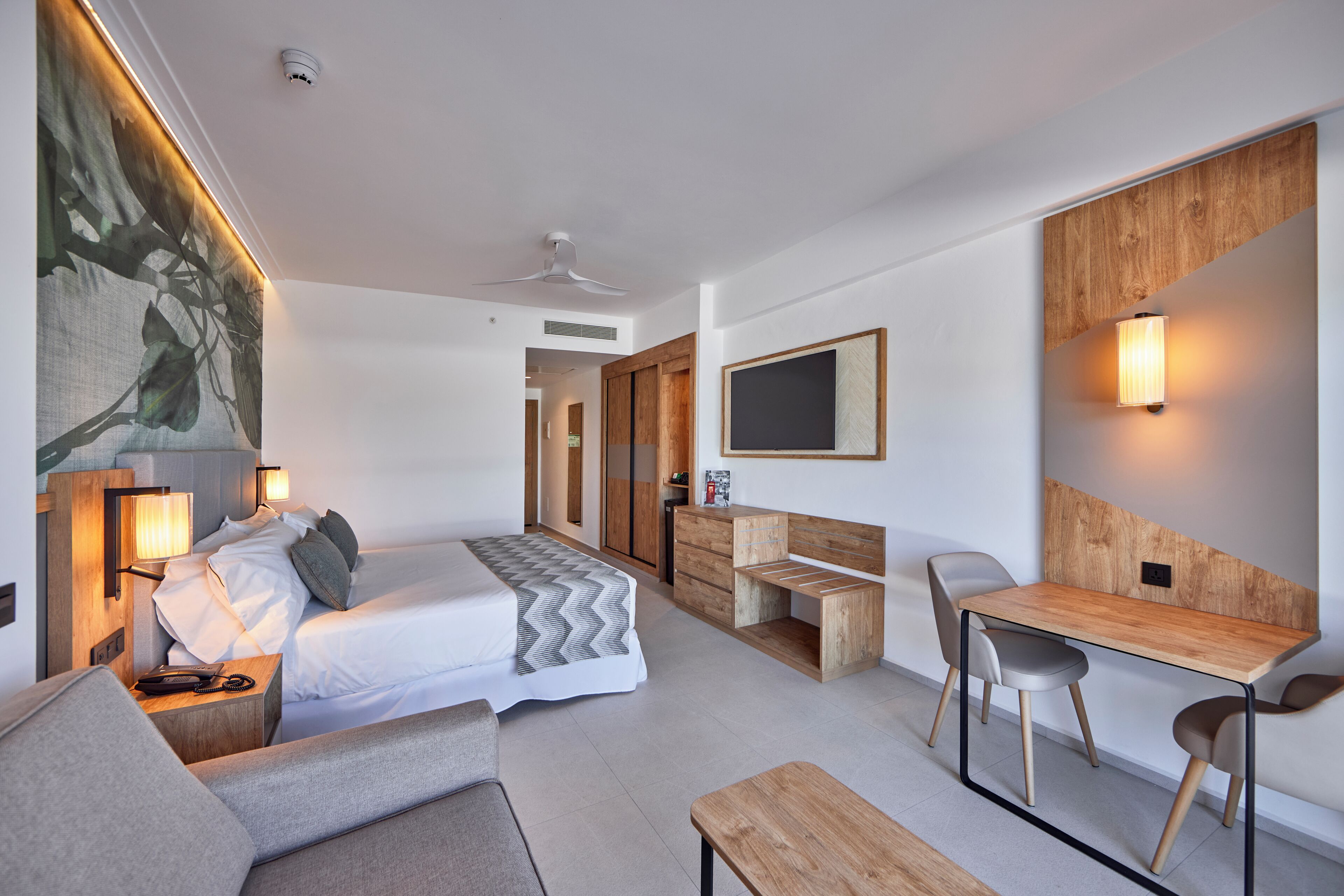 Una habitación de hotel moderna con una cama, un escritorio, una silla, un sofá y un cuadro grande en la pared.