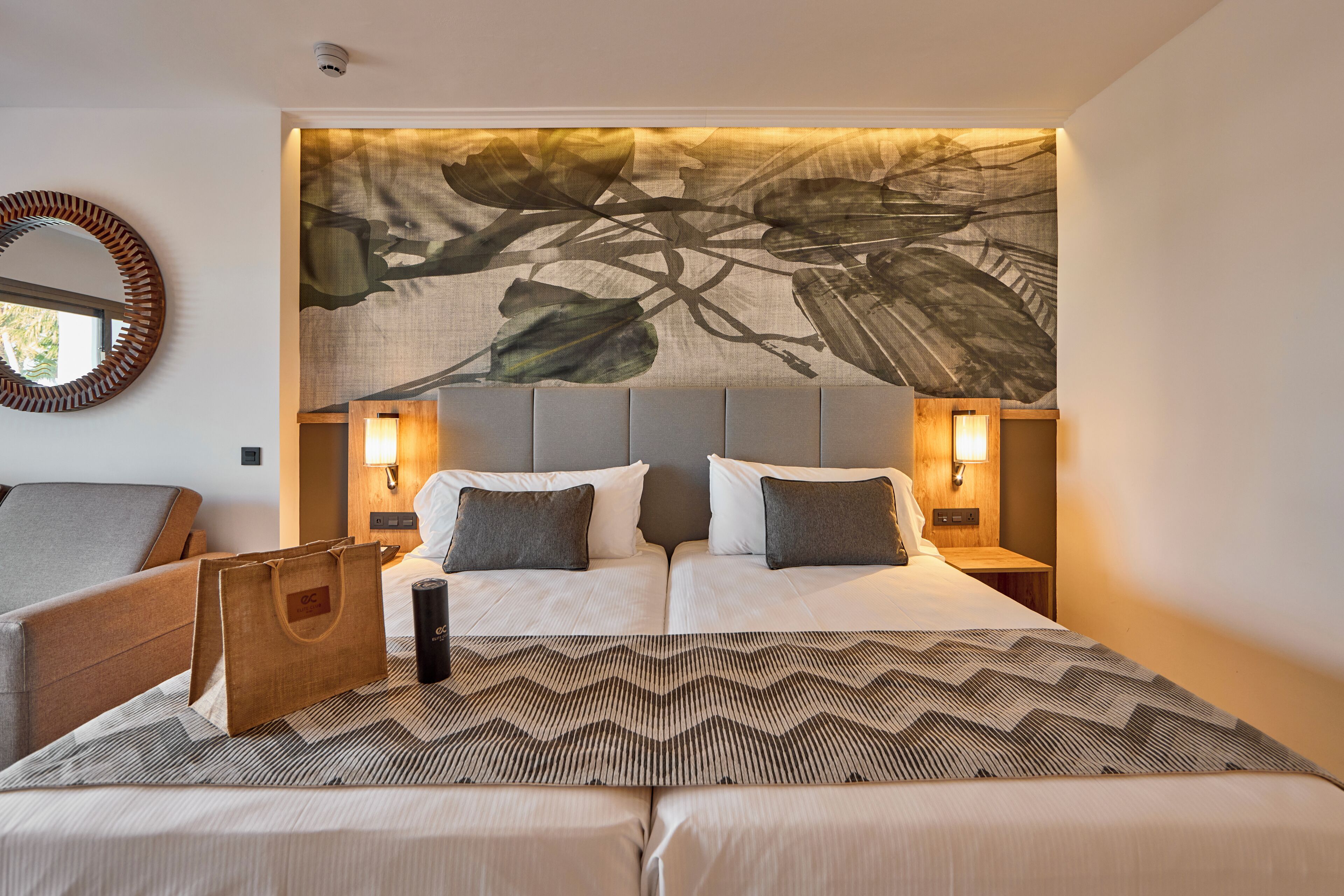 A hotel room with a large bed, two bedside tables with lamps, a round mirror, and a wall-mounted artwork.