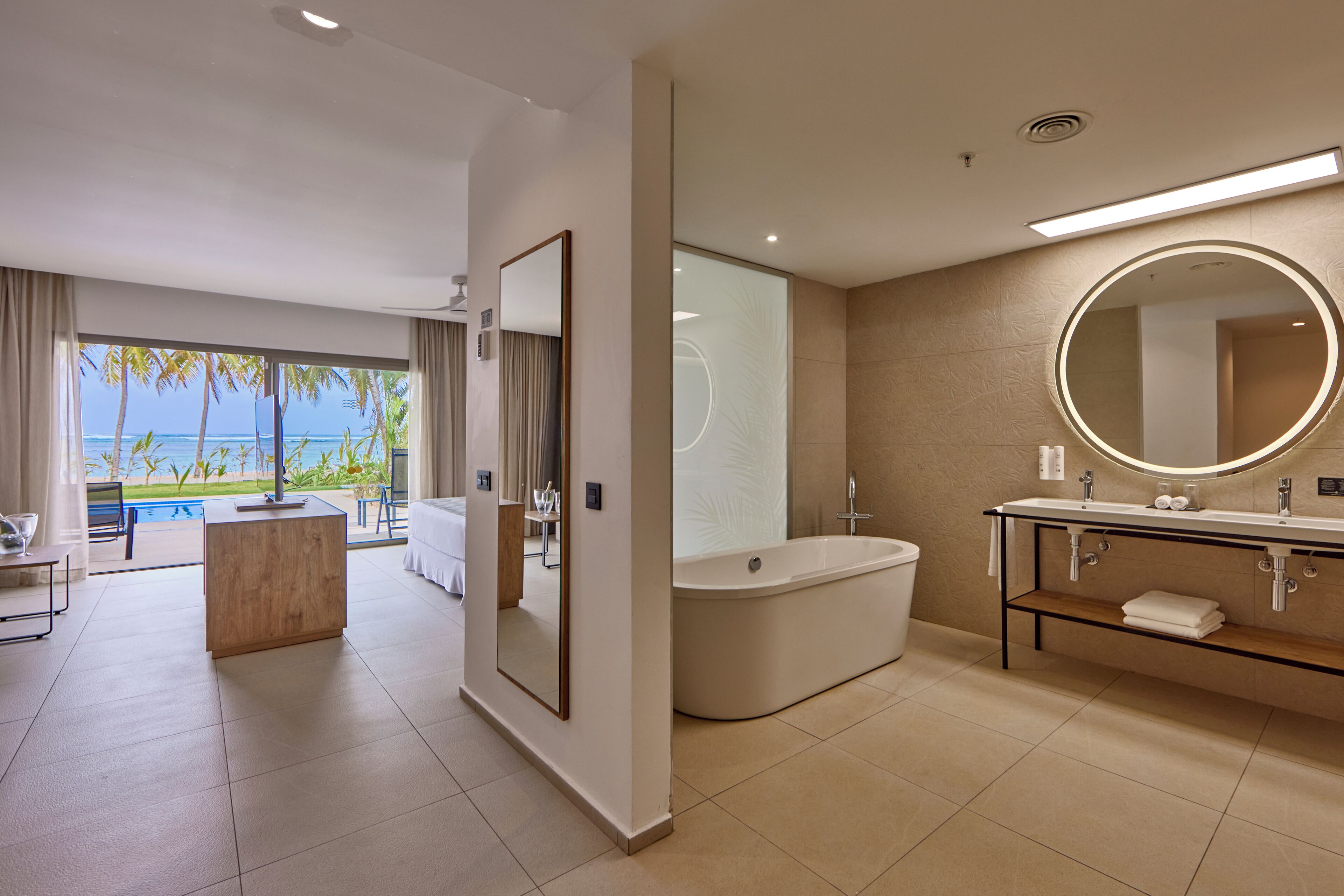 Un baño moderno con bañera, un espejo grande y un tocador con un espejo redondo.