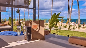 A table with a bottle, two glasses, and a bag, overlooking a beach with palm trees and the ocean. - Hotel Riu Palace Mauritius - All Inclusive - Adults Only (Le Morne)