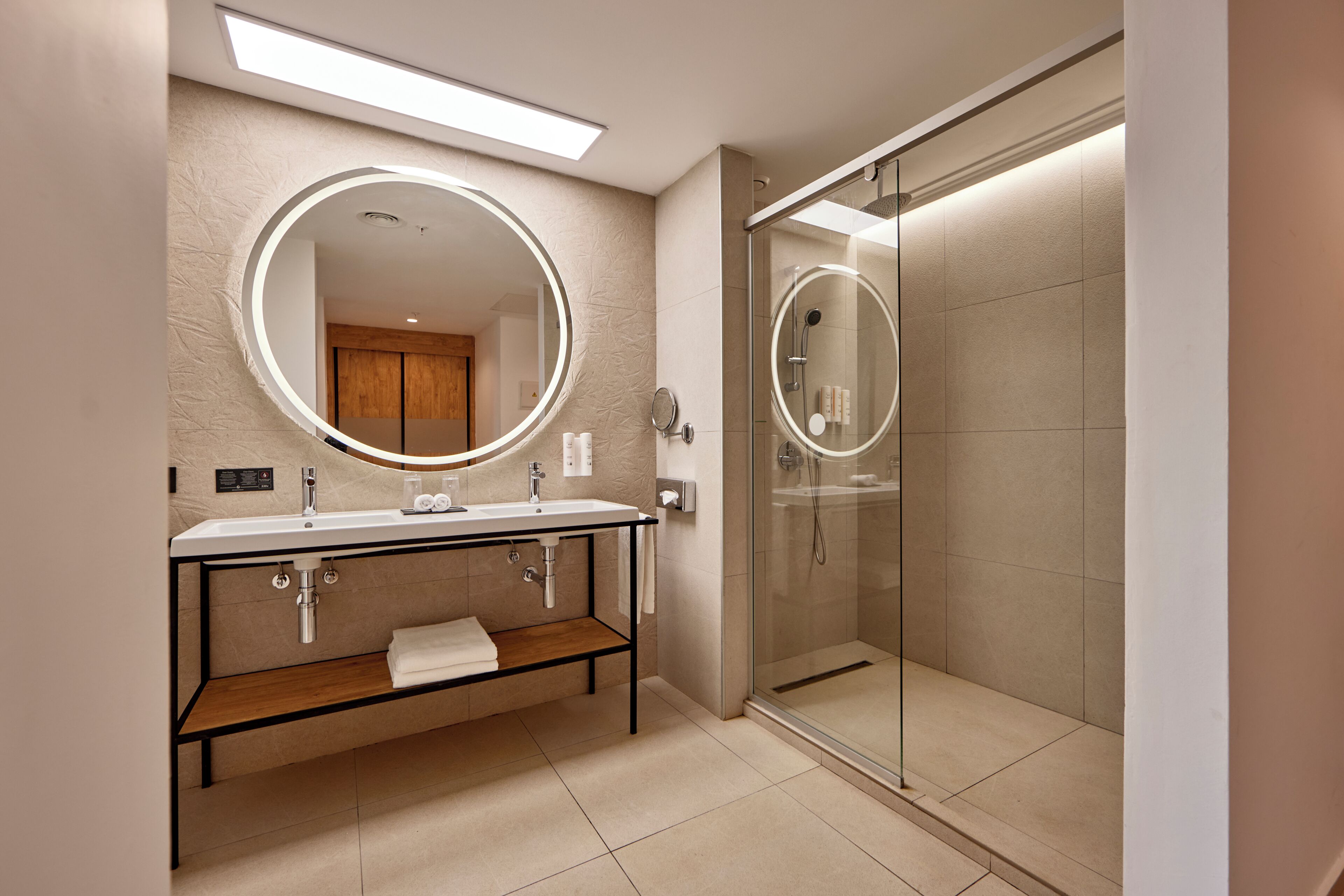 Un baño moderno con un espejo grande, ducha con mampara de vidrio y tocador de madera.